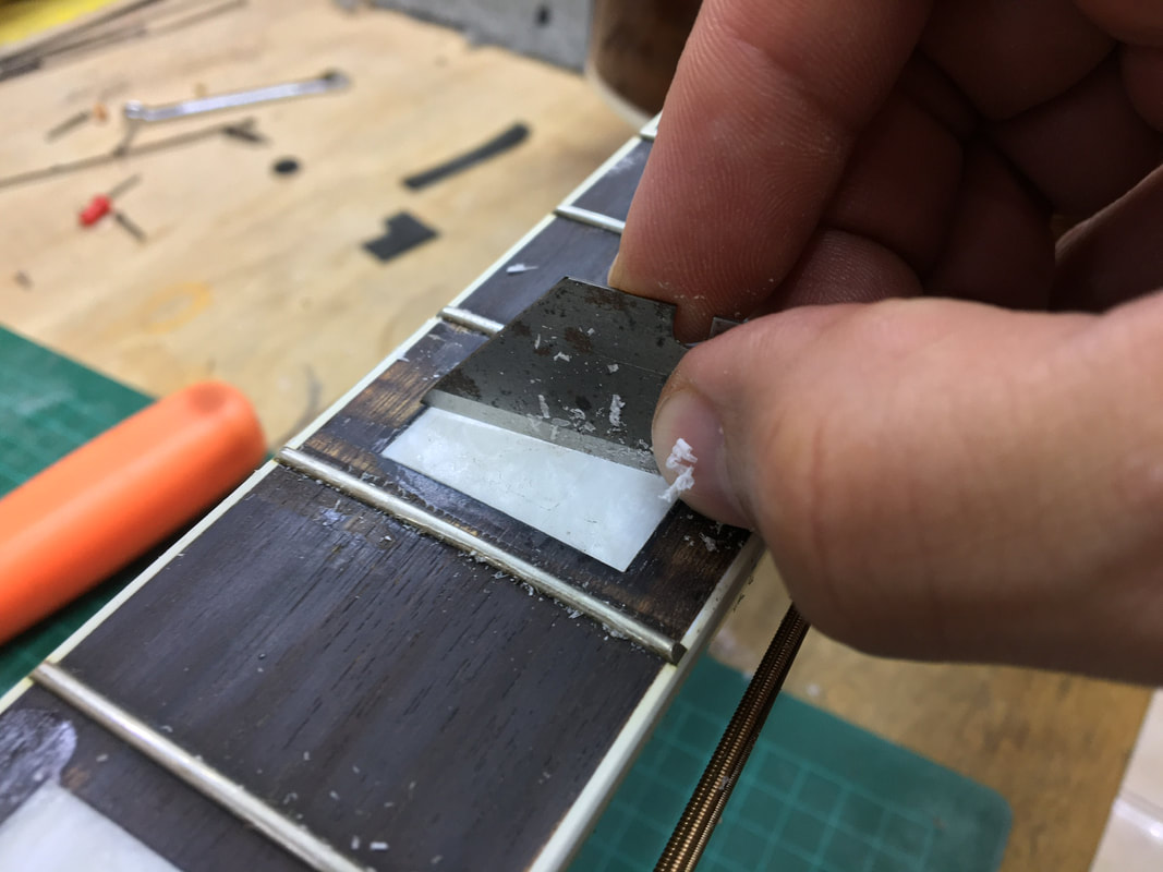 Foto de una navaja siendo utilizada para reparar el diapasón de una guitarra
