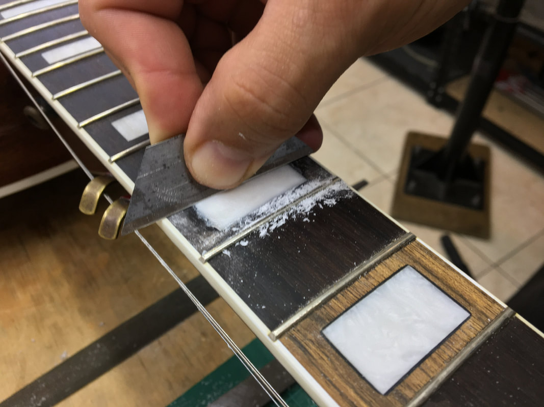 Foto de una navaja cortando la incrustación de un diapasón de guitarra