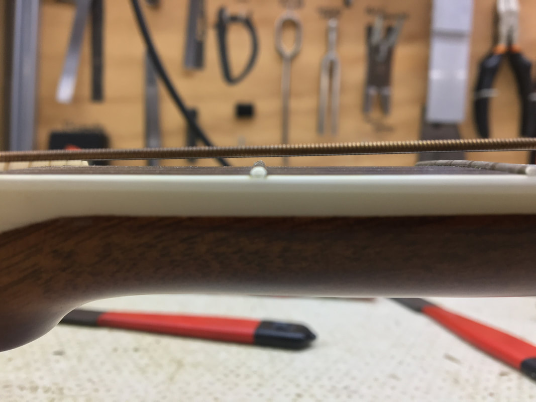 Vista lateral del un mástil de guitarra acústica en el que se pueden observar las cuerdas muy altas sobre el primer traste