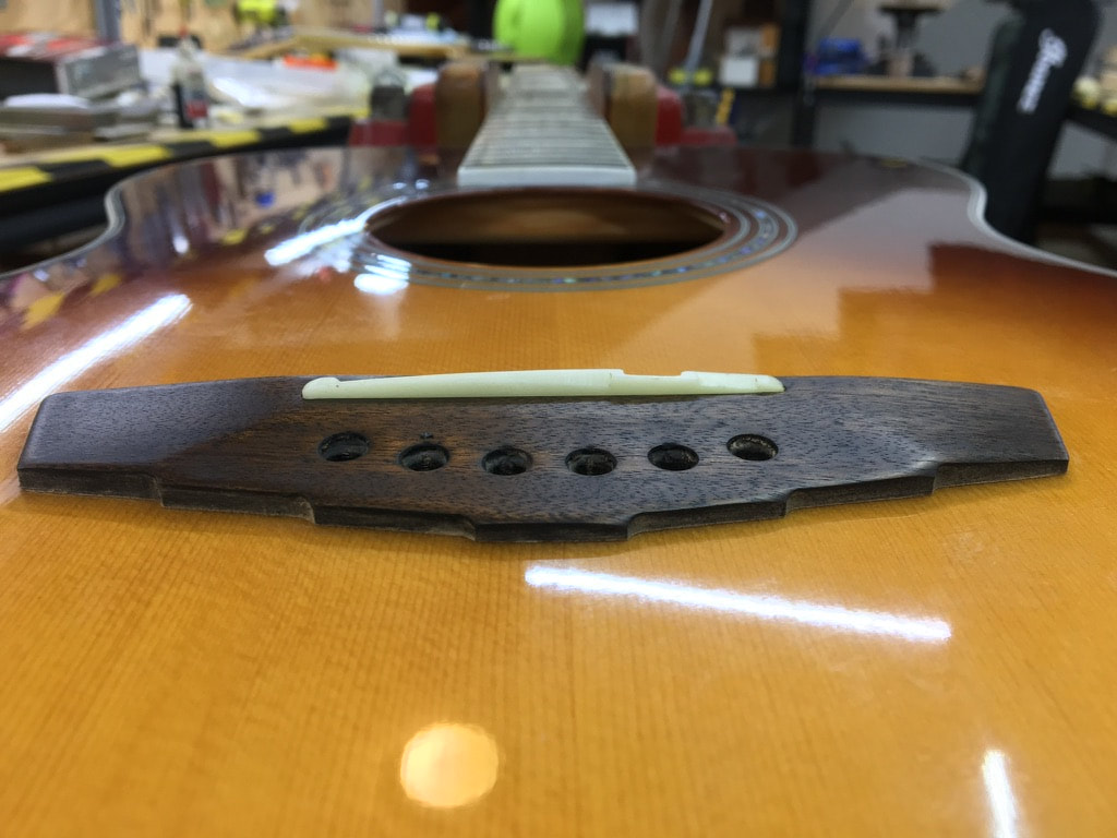Vista posterior del puente de guitarra acústica. Se aprecian en primer plano los pines, el saddle y al fondo la boca y los últimos trastes de la guitarra
