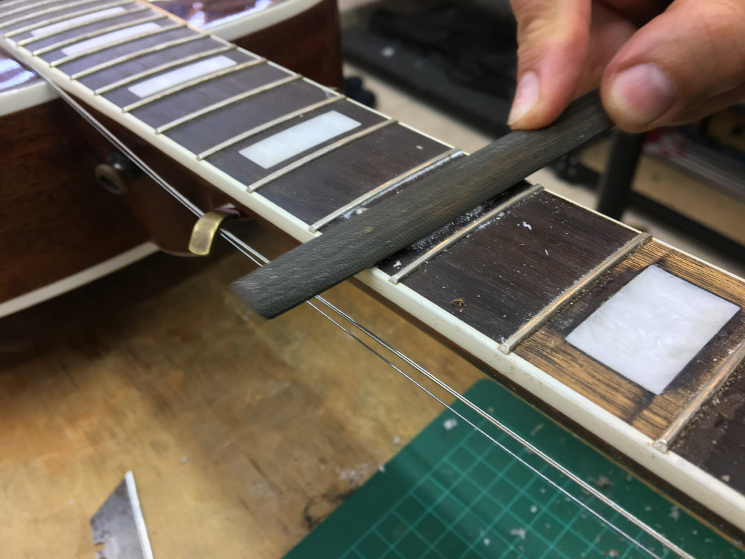 Foto de una lima de media caña siendo utilizada para reparar una incrustación en el diapasón de una guitarra